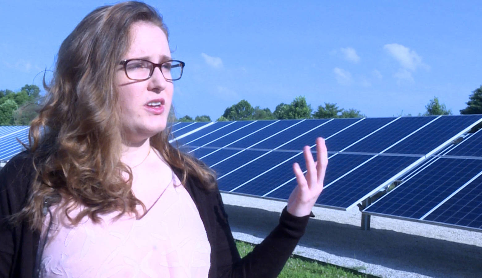 Indiana University student Savannah Rodrigue stands in front of a solar array next to a water booster station in Bloomington which helps to offset some of the station's energy use. (Rebecca Thiele/IPB News)