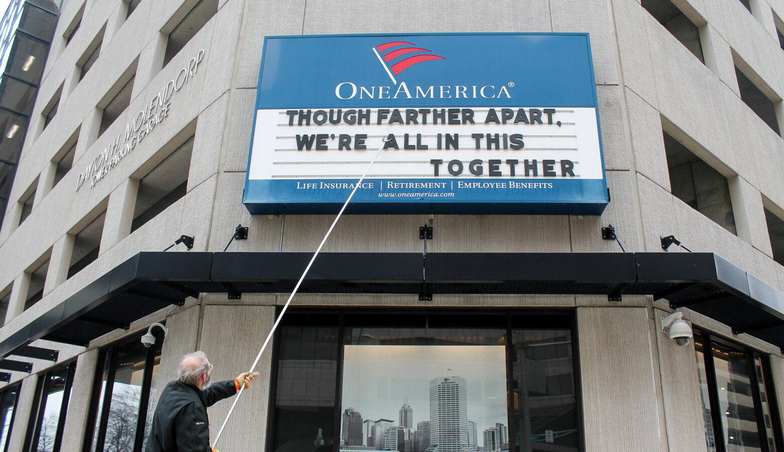 A man adjusts the One America sign in downtown Indianapolis. It usually displays a pun, but the message shortly before the governor's address reads: "Although father apart, we're all in this together." (Lauren Chapman/IPB News)
