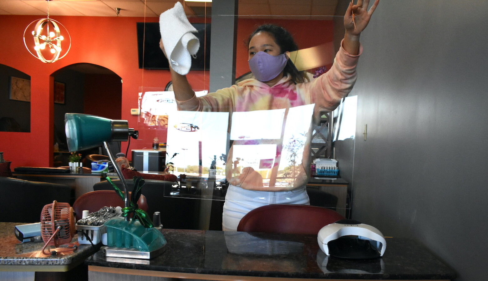 A younger worker at a nail salon cleans a plexiglass shield being used to prevent the spread of COVID-19. (Justin Hicks/IPB News)