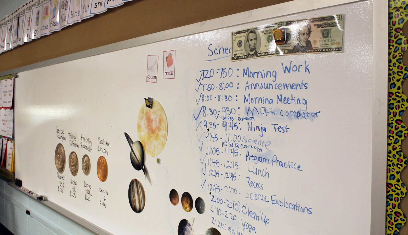 The whiteboard of an elementary school classroom lists the agenda for students along with magnets displaying currency and their values.