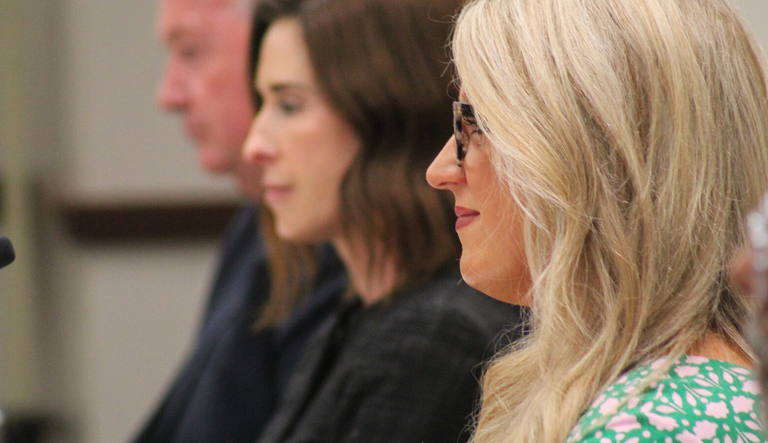 Indiana Secretary of Education Katie Jenner sits next to other State Board of Education board members during a meeting. Jenner has blonde hair and wears glasses. She is smiling at a speaker during a public feedback hearing.