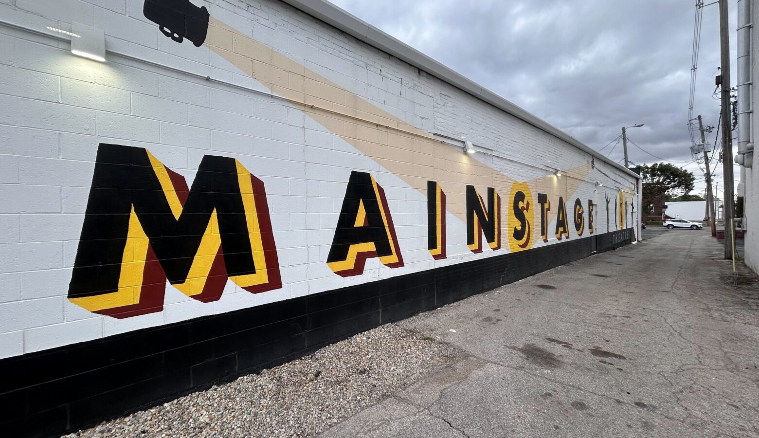 A lettered mural is painted on the outside of a long white building, with the word Mainstage in black and yellow letters.