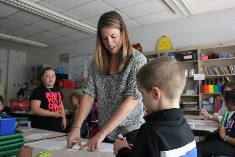 An educator points at a piece of paper in front of a student.