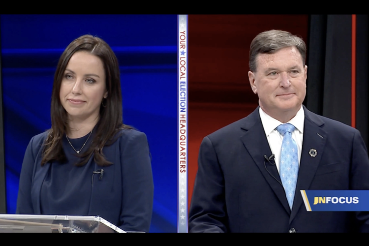 A screenshot of the Indiana attorney general candidate debate. Destiny Wells is a White woman with dark hair. She is wearing a dark blue jacket and top. Todd Rokita is a White man with dark, graying hair. He is wearing a dark blue suit with a white shirt and light blue and white tie.