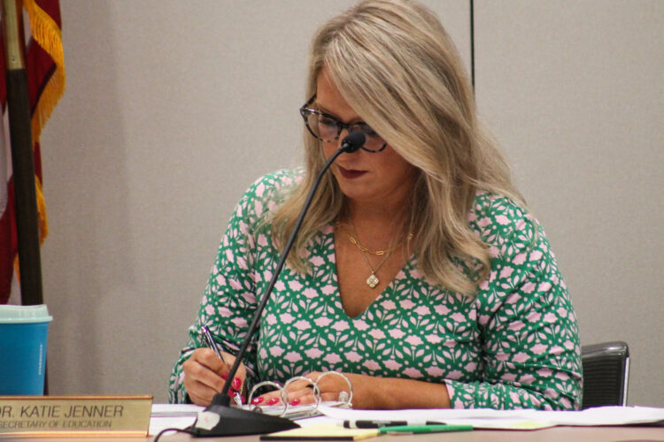 Katie Jenner writes on a piece of paper while sitting in front of a microphone.