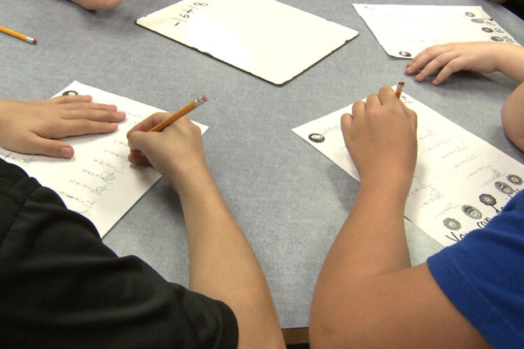 Two students sit at a table and answer math problems.