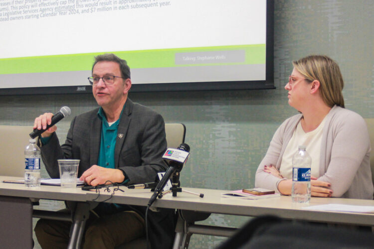 Larry DeBoer is a White man with dark hair. He is wearing glasses and a gray blazer over a green shirt. Neva Butkus is a White woman with blonde hair. She is wearing glasses and a cream sweater over a white top.